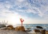 frau-in-roter-sportkleidung-macht-yoga-auf-einem-felsen-am-meer