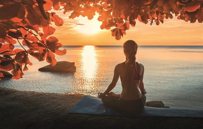 frau-sitzt-am-meer-und-meditiert-im-sonnenuntergang