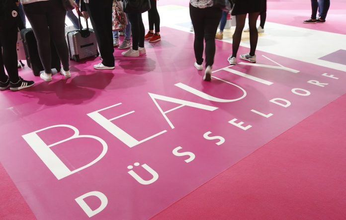 Man erkennt die Beine von Menschen, die über einen rosa farbenen Teppich mit der Aufschrift Beauty Düsseldorf laufen.