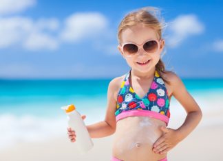 Kleines Mädchen am Meer cremt sich mit Sonnenschutzmittel ein