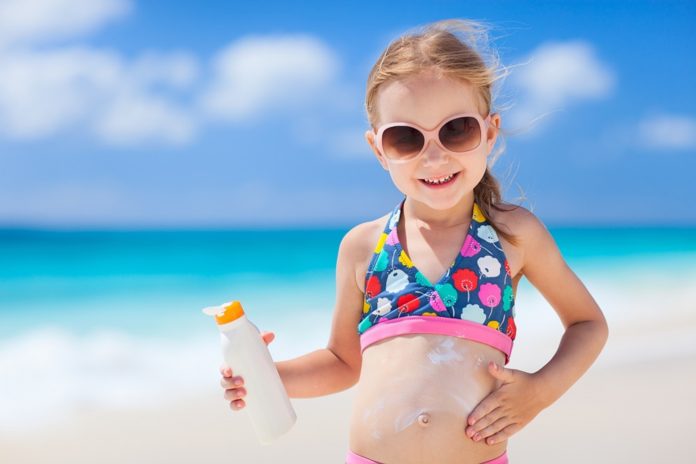 Kleines Mädchen am Meer cremt sich mit Sonnenschutzmittel ein