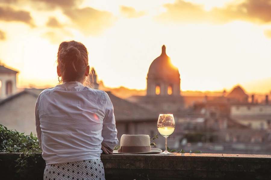 Eine Frau steht an der Balkonbrüstung und schaut auf die Kulisse von Rom.