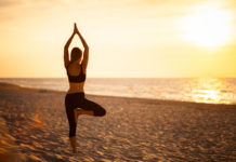 So angesagt sind Wellness- und Health-Reisen im Sommer Frau in Yoga-Position Baum am Strand.