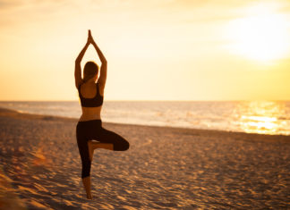 So angesagt sind Wellness- und Health-Reisen im Sommer Frau in Yoga-Position Baum am Strand.