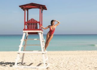 Frau in rotem Badeanzug posiert am Strand auf dem Rettungsschwimmerturm.