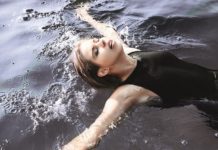 Junge Frau im schwarzen Badeanzug schwimmt auf dem Rücken im Wasser.