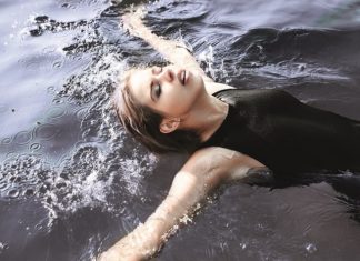 Junge Frau im schwarzen Badeanzug schwimmt auf dem Rücken im Wasser.