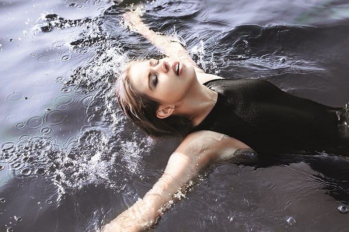 Junge Frau im schwarzen Badeanzug schwimmt auf dem Rücken im Wasser.