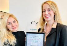Zwei junge blonde Frauen halten eine gerahmte Urkunde gemeinsam in den Händen.