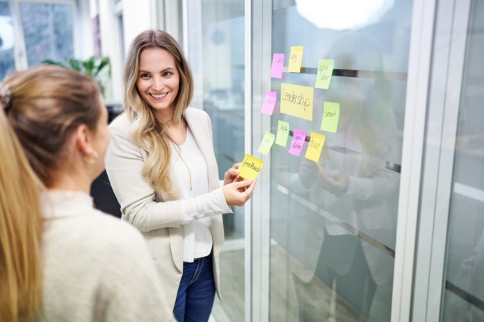 Zwei Frauen stehen vor einer mit Post-Its beklebten Glasfront