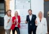 Drei Frauen und ein Mann stehen vor einem übergroßen Charta-Ausdruck. Sie halten Stifte in der Hand.