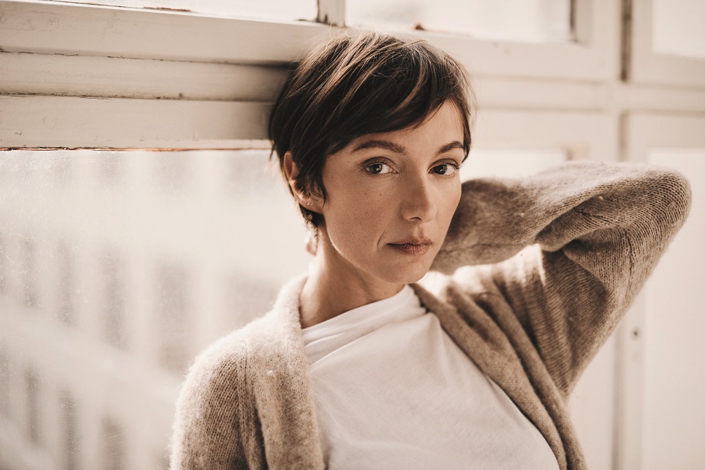 Bild von Schauspielerin Julia Koschitz an einen Fensterrahmen lehnend.