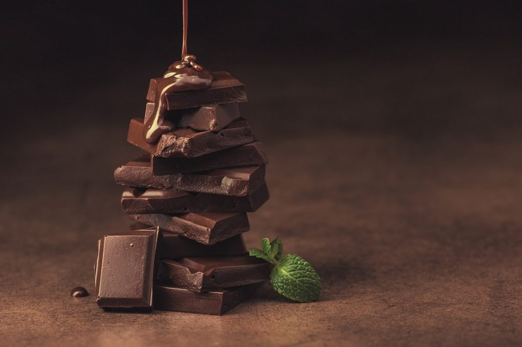 melted chocolate pouring into a piece of chocolate bars with green mint leaf on a table