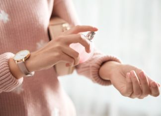 Eine Fru im rosa Pullover besprüht ihr Handgelenk mit einem Duft aus einem Zerstäuber, den sie in der anderen Hand hält.