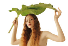 Junge Frau mit langen Haaren hält ein großes Blatt wie einen Schirm über sich.