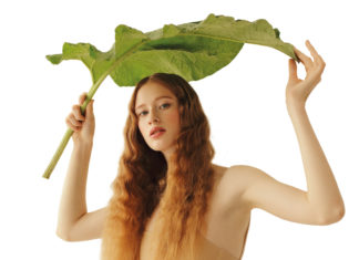 Grün ist Trumpf Junge Frau mit langen Haaren hält ein großes Blatt wie einen Schirm über sich.