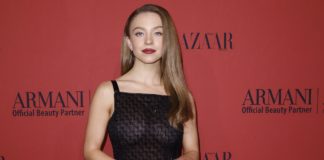 Sydney Sweeney auf der Berline. Sie tägt ein schwarzes Trägerkleid und steht vor einer roten Wand.