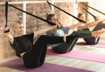 Drei junge Frauen auf Yogamatten beim Barre-Workout mit Bändern