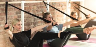 Drei junge Frauen auf Yogamatten beim Barre-Workout mit Bändern