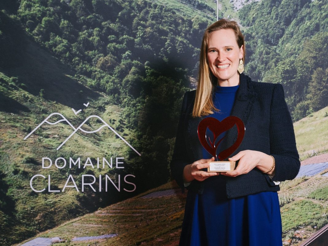Eine Frau mit langen Haaren hält den Clarins Prix in den Händen.