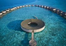 Ein rundes Gebäude, über einen Steg erreichbar liegt umgeben von türkisfarbenem Wasser.