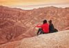 Zwei junge Frauen sitzen auf einer Felserhöhung in der Wüste und bewundern den Sonnenaufgang.