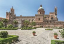 Bild von der Kathedrale von Palermo. Ein großer Bau mit blauer Kuppel. Davor ein gepflasterer Platz mit Blumenkübeln und Parkanlage.