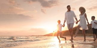 Happy family running on sandy beach near sea at sunset, space for text. Banner design