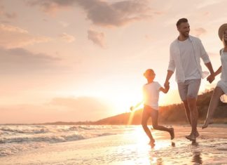 Happy family running on sandy beach near sea at sunset, space for text. Banner design
