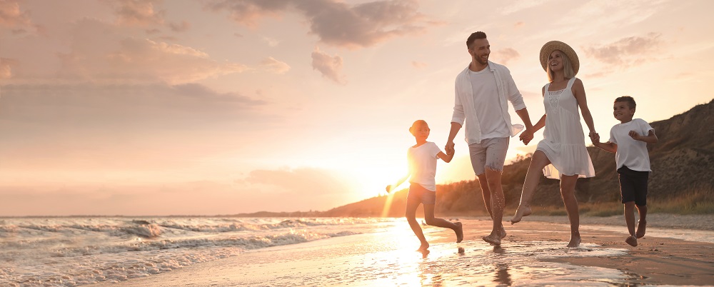 Happy family running on sandy beach near sea at sunset, space for text. Banner design