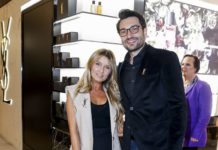 Neuer YSL Beauty Counter im KaDeWe Eine Frau mit langen blonden Haaren und ein größerer Mann, beide in festlicher Kleidung, stehen vor einem Verkaufsregal und blicken in die Kamera.