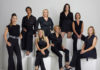Eine Gruppe von Frauen, alle sind schwarz gekleidet, steht oder sitzt auf weißen Blöcken.