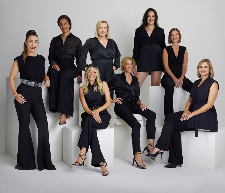 Eine Gruppe von Frauen, alle sind schwarz gekleidet, steht oder sitzt auf weißen Blöcken.