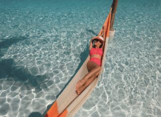 Junge Frau in Bikini liegt in einer Hängematte über dem Meer.