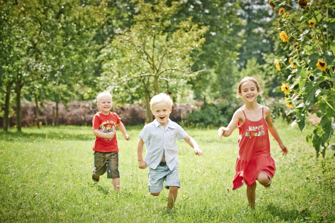 Drei Kinder rennen über eine Streuobstwiese.