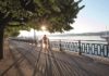 Frau in Bustier und kurzer Hose joggt im Sonnenschein entlang der Uferpromenade des Genfersees.