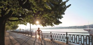 Frau in Bustier und kurzer Hose joggt im Sonnenschein entlang der Uferpromenade des Genfersees.