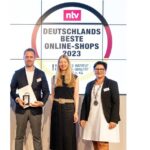Zwei Frauen und ein Mann, alle in schicker Kleidung blicken n die Kamera. Der Mann hält eine Auszeichnung in den Händen.