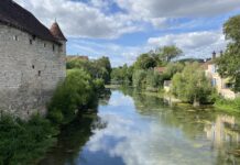 Blick auf einen Flußlauf, gesäumt von einer alten Mauer und Bewuchs. Der Himmel spiegelt sich im Wasser