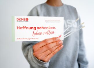 Weltkrebstag: DKMS ruft zur Registrierung auf Eine Hand hält ein weißes Papier mit einer roten Aufschrift und drei Abstrichtupfern.