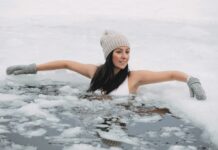 Eine junge mit Mütze und Handschuhen badet im Eisloch eines zugefrorenen Sees.