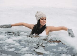 Für die Gesundheit ins kalte Wasser – EisFlow Retreat im Klosterhof Alpine Hideaway & Spa Eine junge mit Mütze und Handschuhen badet im Eisloch eines zugefrorenen Sees.