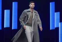 Kai Havertz ist eines der neuen Gesichter der BOSS Bottled Triumph Elixir Kampagne Junger Mann im Trenchcoat vor dunklem Hintergrund mit blau beleuchteten Lichtbalken