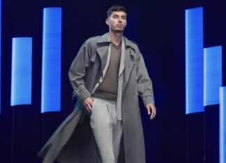 Kai Havertz ist eines der neuen Gesichter der BOSS Bottled Triumph Elixir Kampagne Junger Mann im Trenchcoat vor dunklem Hintergrund mit blau beleuchteten Lichtbalken