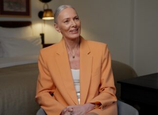 Estée Lauder startet die #becauseofmyage-Kampagne Eine Frau mit weißen Haaren und apricotfarbenem Blazer sitzt auf einem Stuhl.