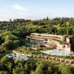 Garten der Sinne – A-ROSA eröffnet erstes Hotel in Italien Blick auf ein Hotelgebäude mit Pool, eingebettet in einen grünen Hügel.
