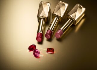 Verschmäht, Verboten, Verehrt Drei in unterschiedlichen Rottönen gehaltene Lippenstifte in goldener Hülle. Drei ebenfalls rote Edelsteine liegen davor.