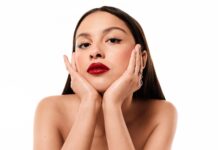 Olivia Rodrigo ist neue globale Lancôme-Markenbotschafterin Junge Frau mit rot geschminkten Lippen und langen dunklen Haaren, hat ihr Gesicht in den Händen aufgestützt und blickt in die Kamera.