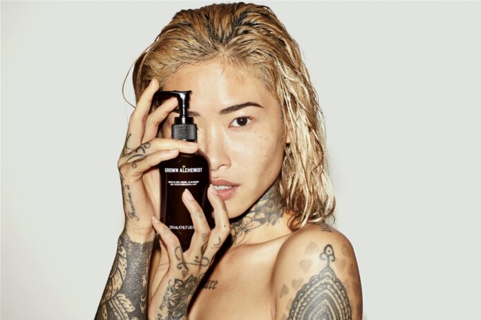 Junge Asiatin mit blondierten Haaren hält ein Produkt von Grwon Alchemist in die Kamera.