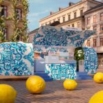 Dolce&Gabbana lädt zur Light Blue Summer Tour Türkis bemalter Anhänger steht vor einem Gebäude. Im Vordergrund liegen mehrere große Zitronen.